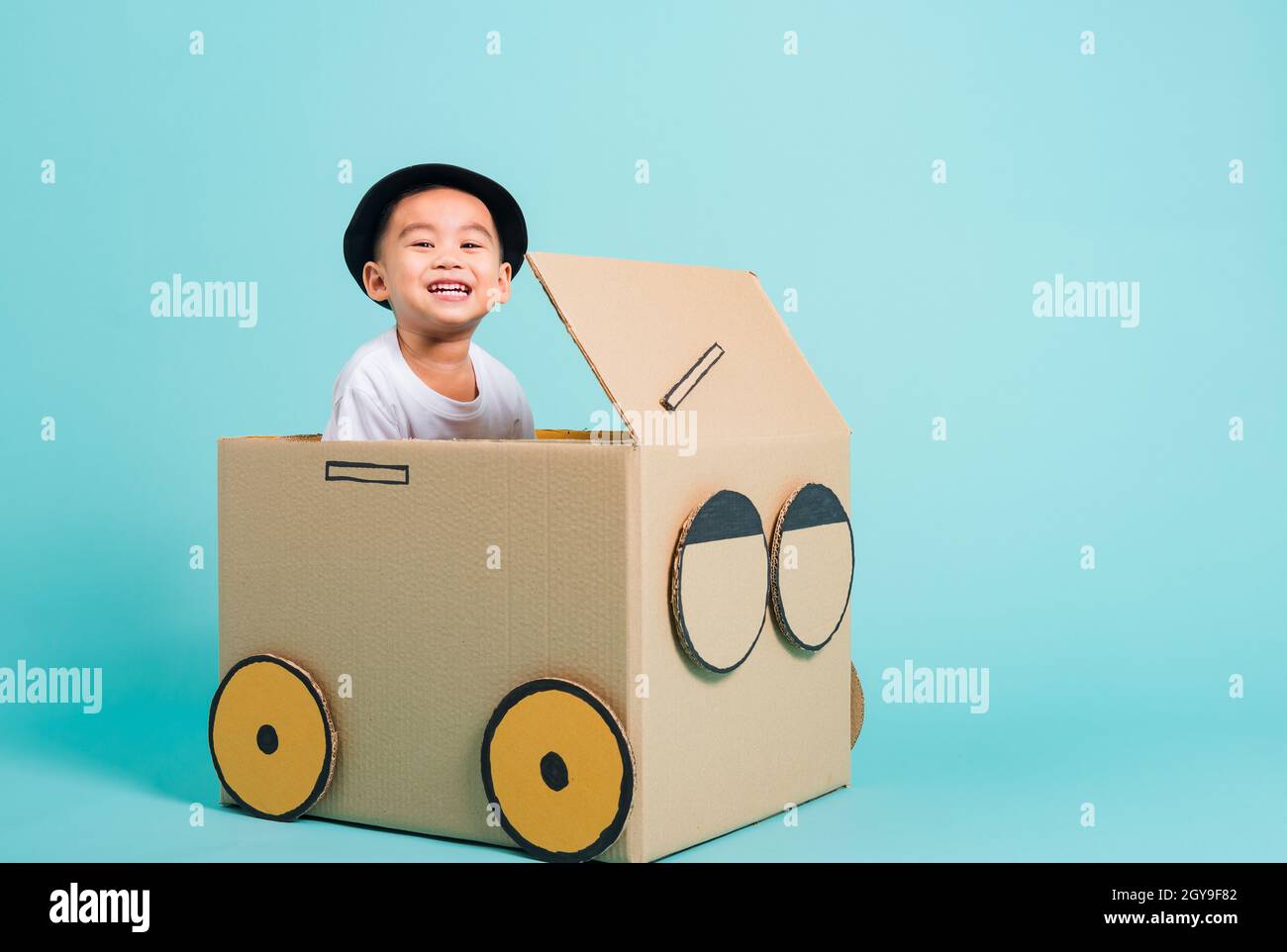 Fröhliche asiatische Kinder Junge lächeln beim Fahren Spielauto kreativ durch eine Pappkartonvorstellung, Sommerferienreisekonzept, Studio auf blauem Backgrot gedreht Stockfoto