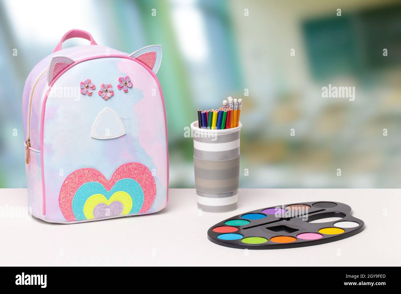 Zurück zur Schule. Farbenfrohe Schulausrüstung und ein heller Schulrucksack auf weißem Tisch über einem abstrakten, verschwommenen Klassenhintergrund. Konzept von Educa Stockfoto