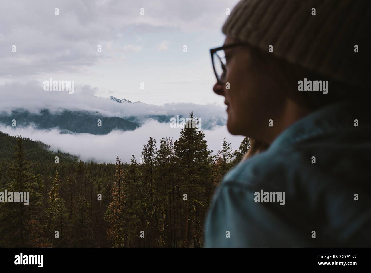 Eine Frau mit Beanie und Brille blickt aus dem Fenster auf die Berge Stockfoto