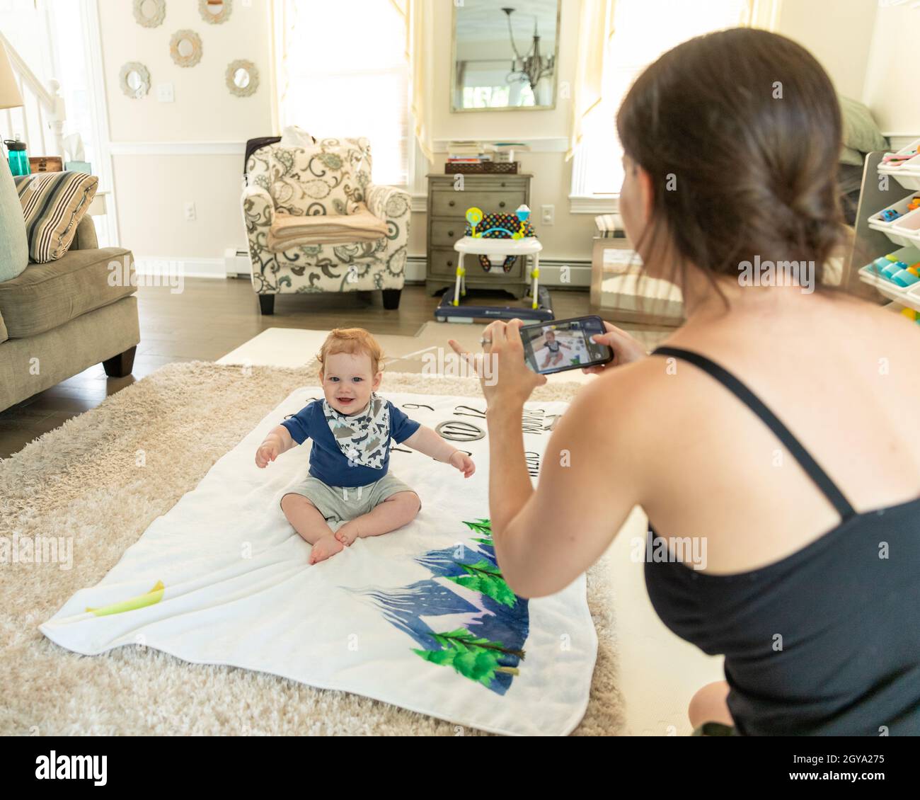 Kleiner Junge, der auf einer Decke sitzt und lächelt, während die Mutter fotografiert. Stockfoto