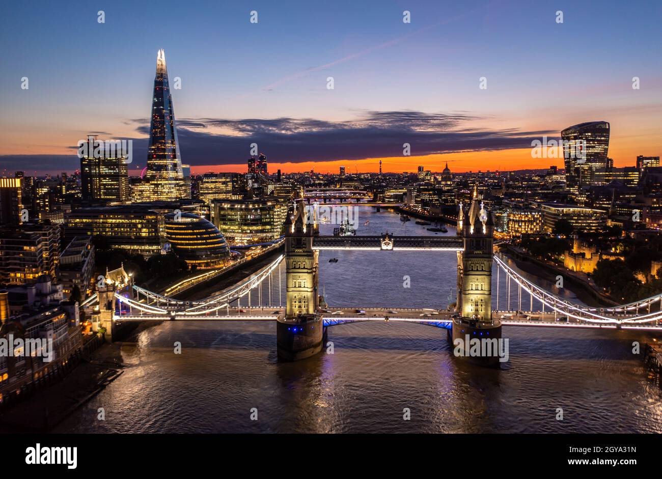 Luftaufnahme der berühmten Tower Bridge über dem Ozean, umgeben von Gebäuden und Wolkenkratzern, unter einem bewölkten Sonnenaufgang am Morgen mit dem Dreiecksgebäude Stockfoto