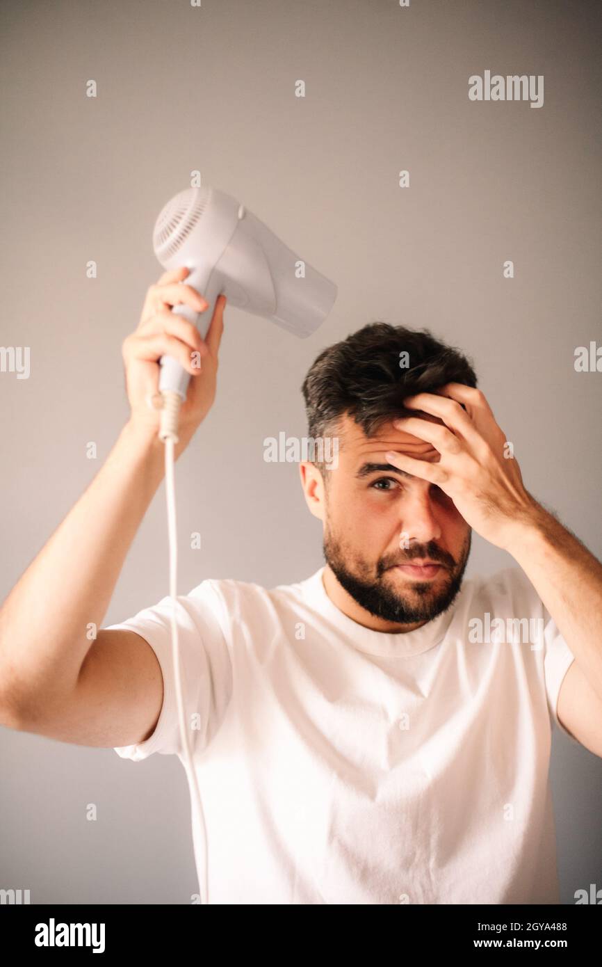 Mann blasen trocknende Haare zu Hause gegen die graue Wand Stockfoto