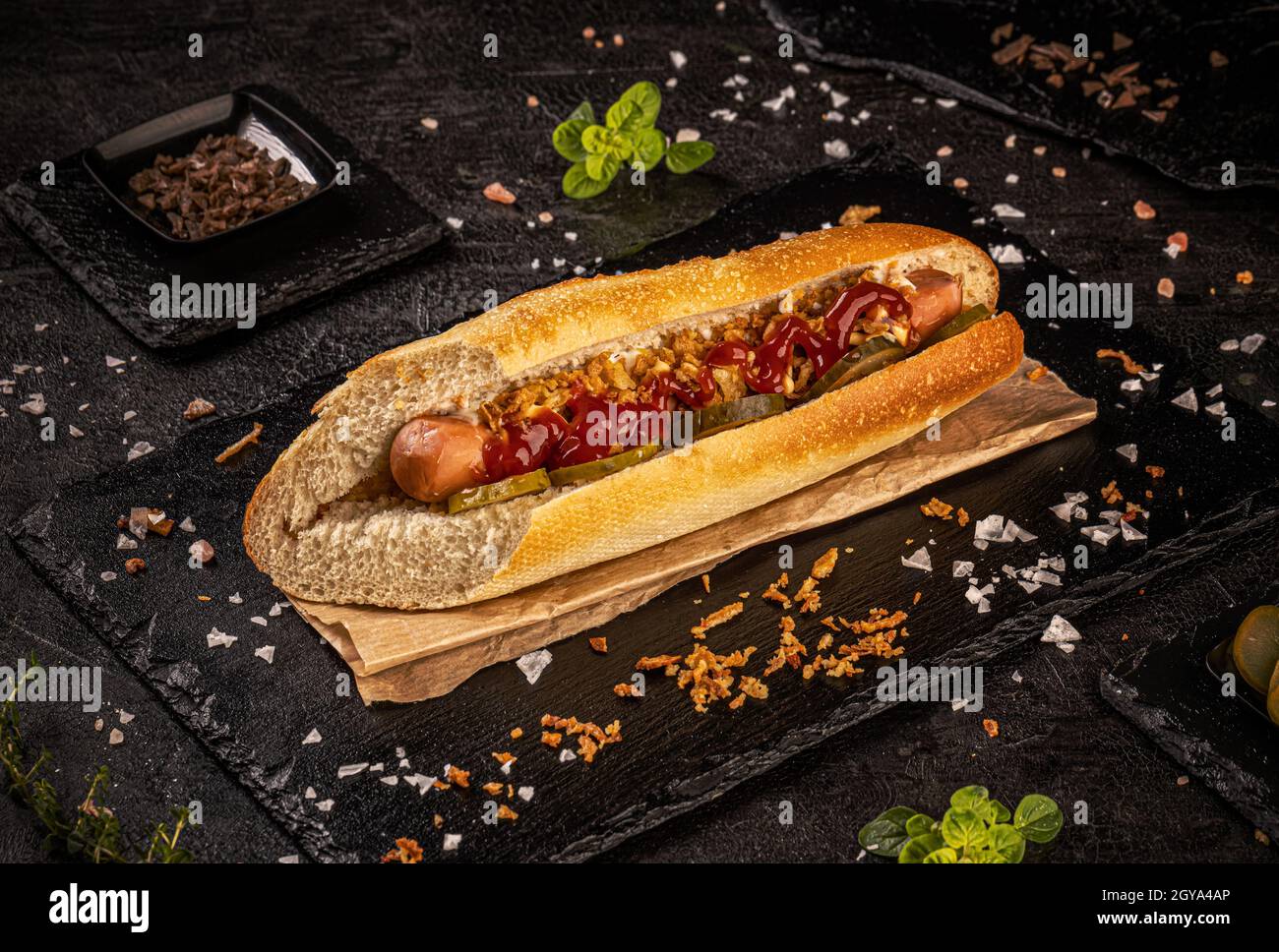 Köstlicher Hot Dog mit Gurken, getrockneten Zwiebeln und Ketchup auf schwarzem Schiefergrund, Stillleben Stockfoto