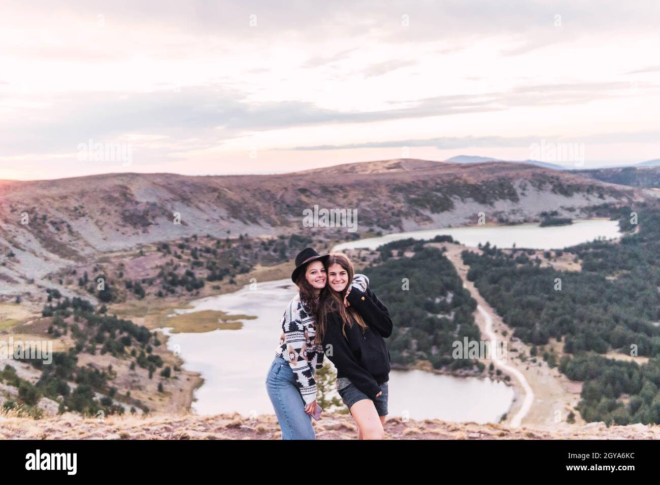 Zwei Frauen umarmen sich und stehen neben einer Seenlandschaft mit Bergen Stockfoto