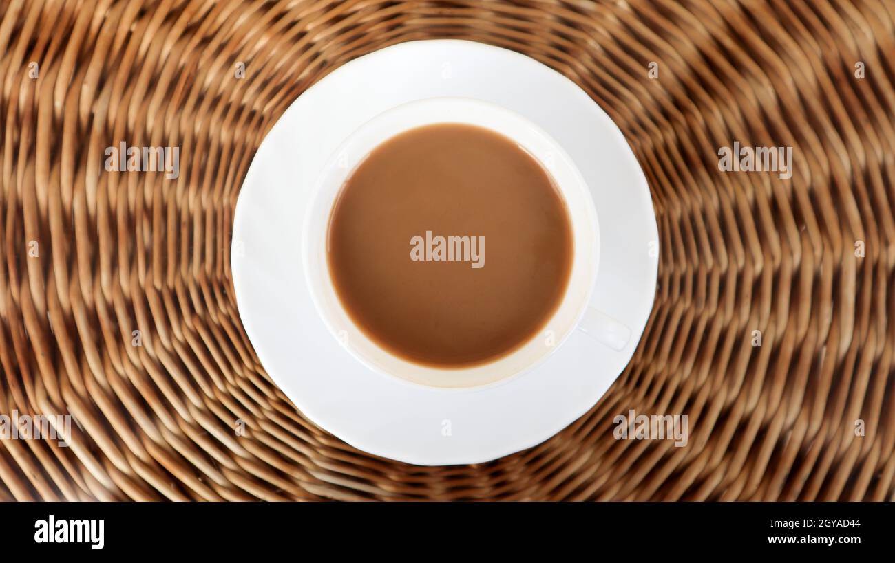 Kaffeetasse auf dem Korbhintergrund, Draufsicht. Heißer aromatischer Kaffee mit Milch. Frisch zubereitetes Getränk wird in einer modernen Tasse auf einem leichten Korbtisch serviert. Stockfoto