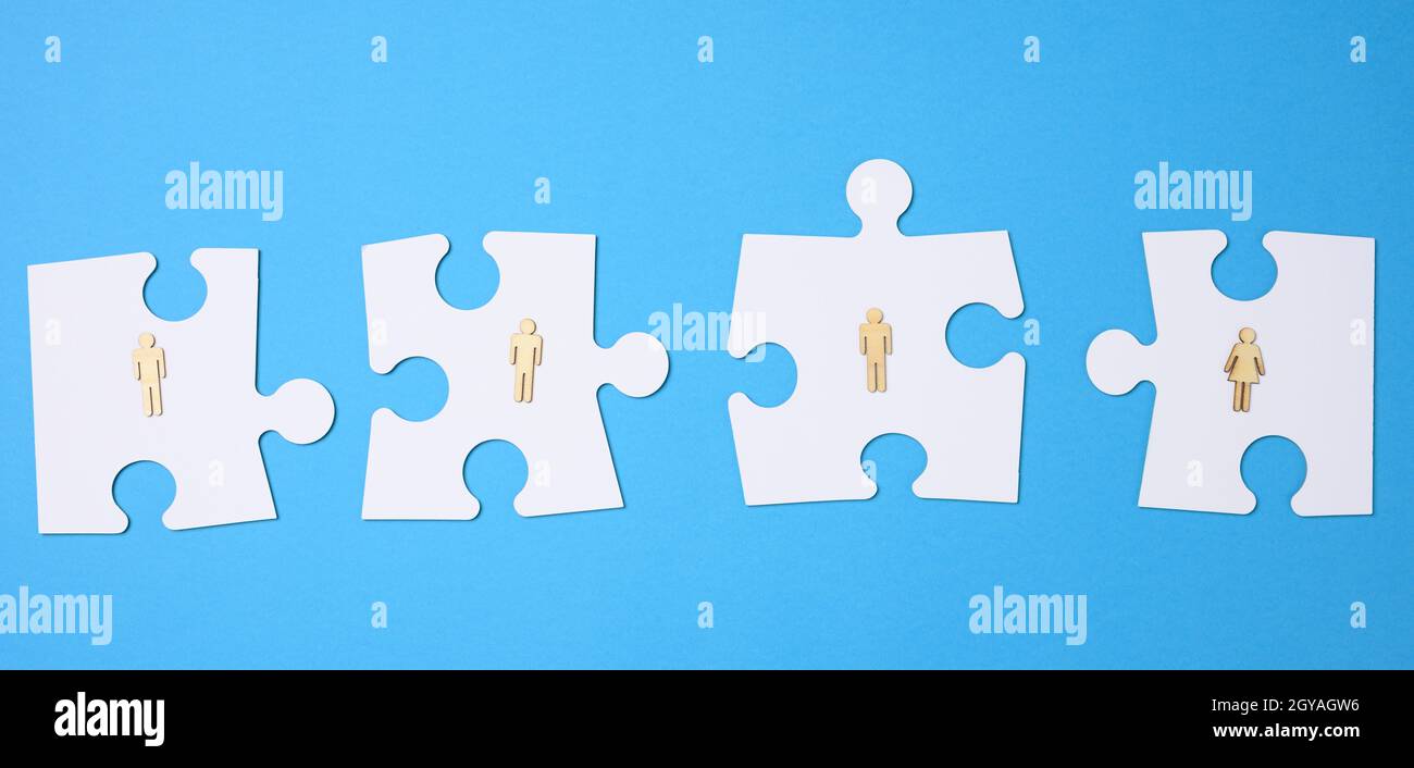 Weiße Puzzles und hölzerne Männer auf blauem Hintergrund. Personalauswahlkonzept, Teamkompatibilität, Individualität jedes Mitarbeiters. Teamarbeit Stockfoto