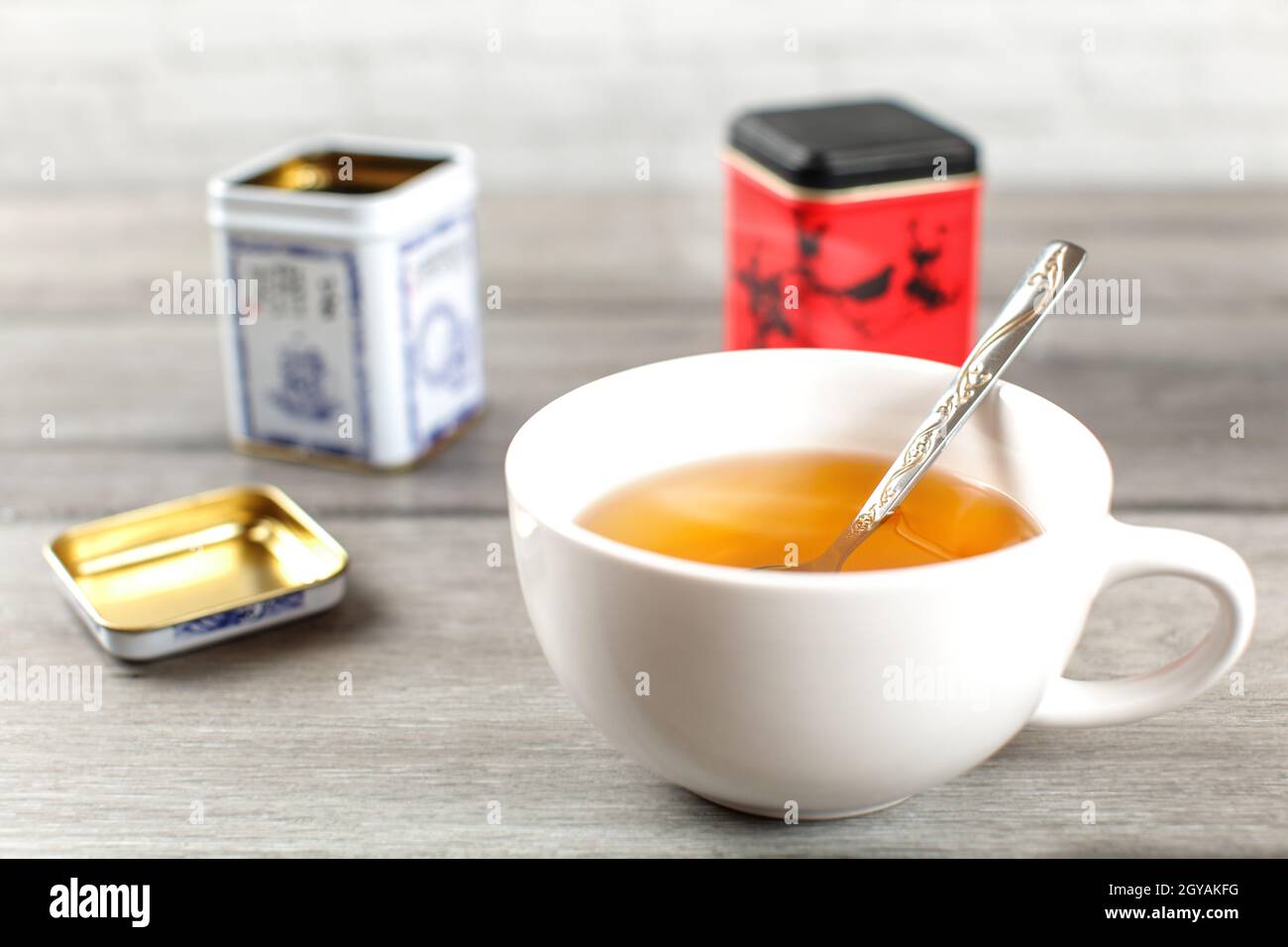 Heiße Tasse schwarzen Tee, mit Metall loses Blatt Caddy im Rücken, auf grau Holzschreibtisch. Stockfoto