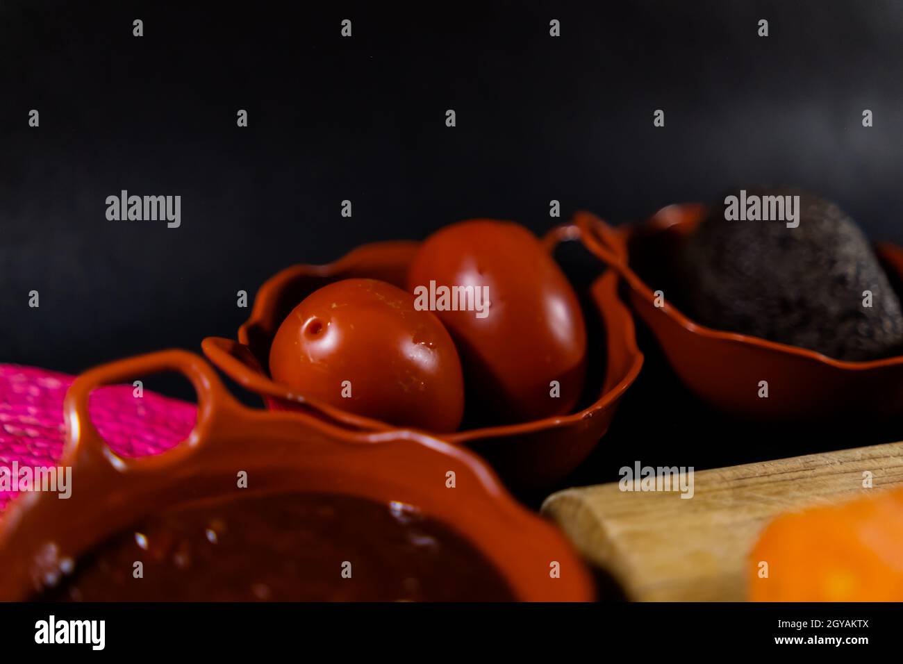 Heiße Sauce, Tomaten und Avocado in Tontöpfen mit schwarzem Hintergrund Stockfoto