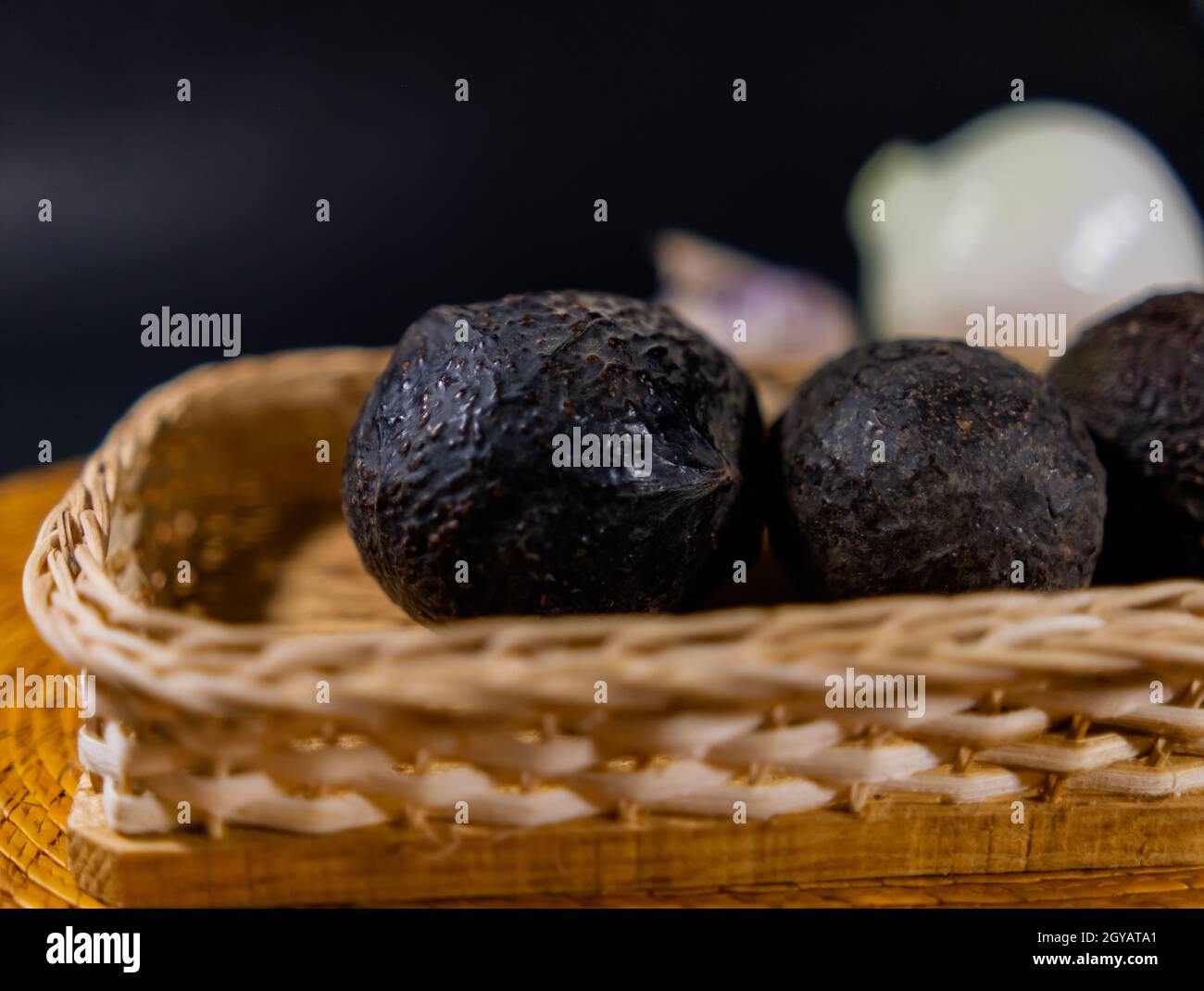 Drei Avocados im traditionellen Palmkorb mit verschwommenem schwarzem Hintergrund Stockfoto