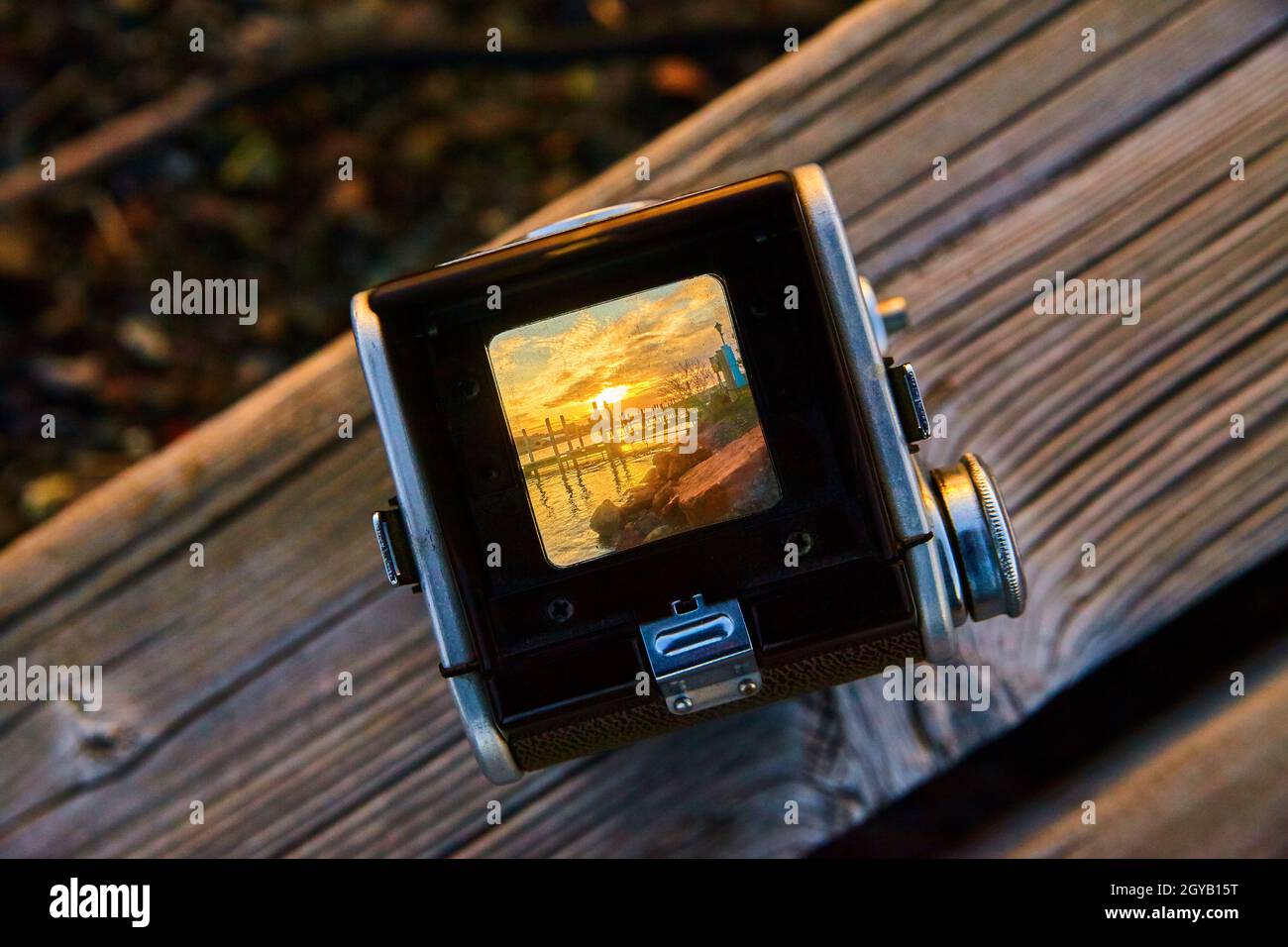 Goldener Sonnenaufgang mit roten Felsen und Docks, gesehen durch eine alte Kamera, die auf einem Holzbrett ruht Stockfoto