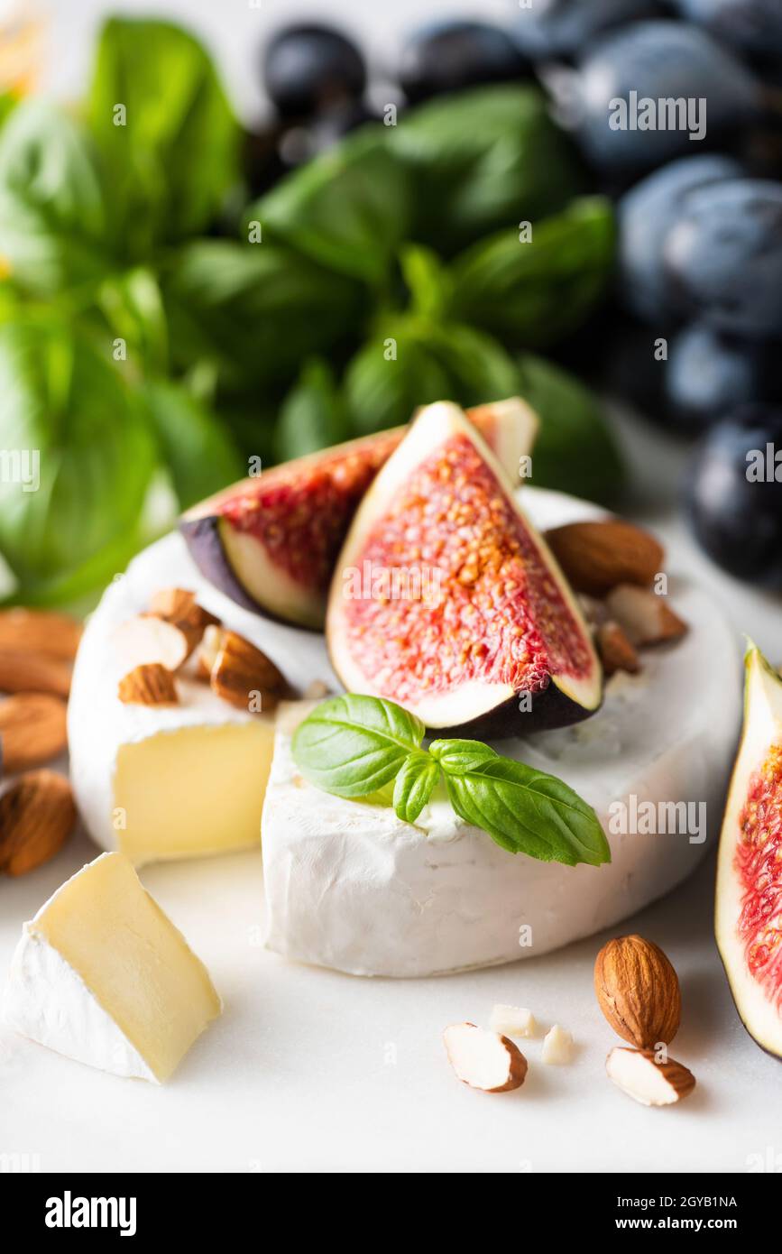 Camembert Käse mit Feigen, Trauben, Nüssen und Basilikum auf weißem Marmorboden, Nahaufnahme Stockfoto