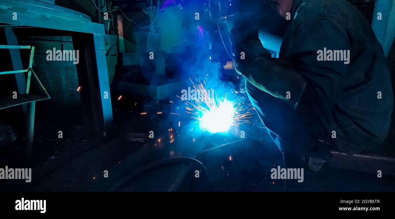 Schweißer schweißen Metall mit Argon-Lichtbogen-Schweißmaschine und hat Schweißfunken. Ein Mann trägt Schweißmaske und Schutzhandschuhe. Sicherheit in der Industrie Stockfoto