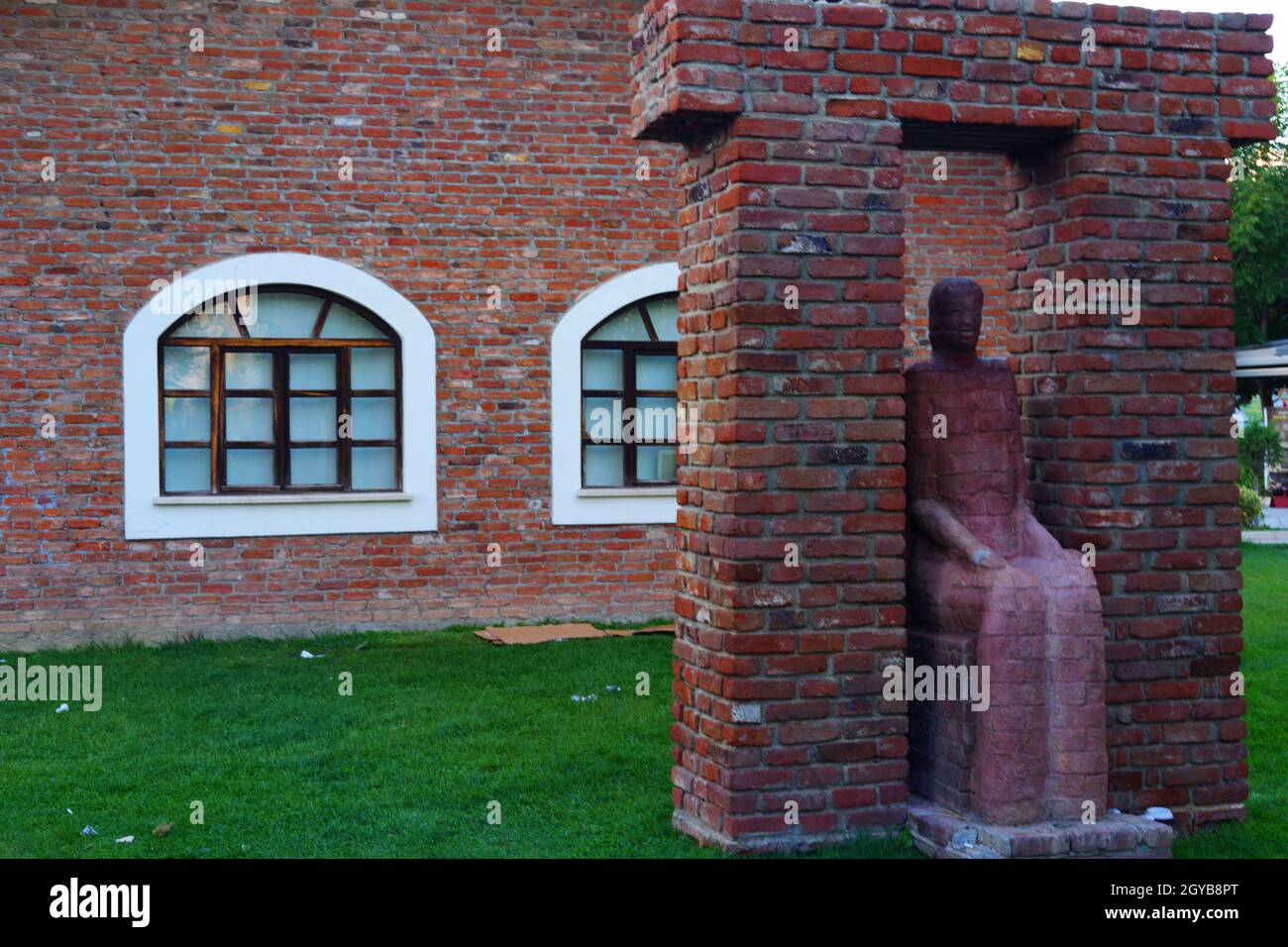 Surrealistische sitzende Frau Skulptur und Ziegelwand im Hintergrund im Freien Stockfoto