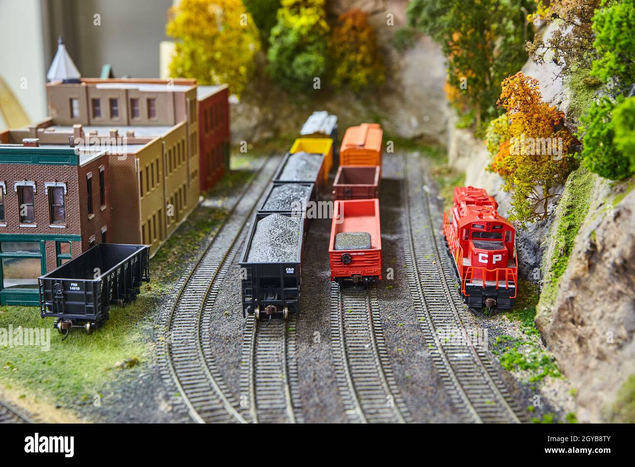 Einige Miniatur-Spielzeugzüge, die Waren auf Bahngleisen neben dem alten westlichen Dorf befördern Stockfoto