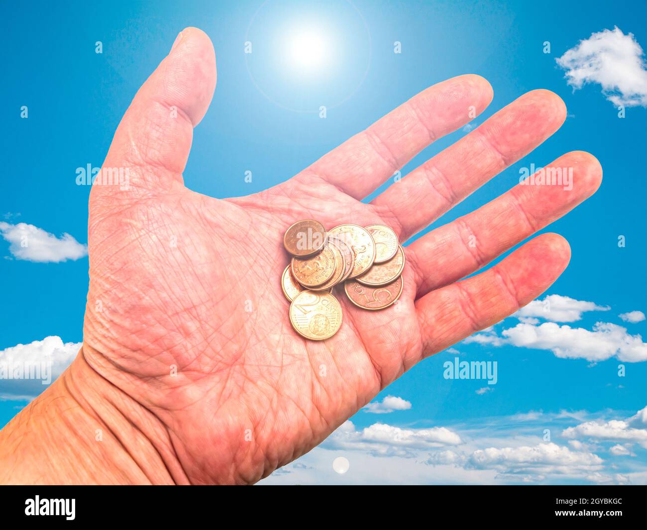 Hand mit Geldmünzen auf einem Hintergrund des blauen Himmels. Gottes Geschenk. Gebet. Bitte um Hilfe. Um Geld bitten. Hand des Gebers. Sonnenstrahlen. Euro-Geld. Backgro Stockfoto