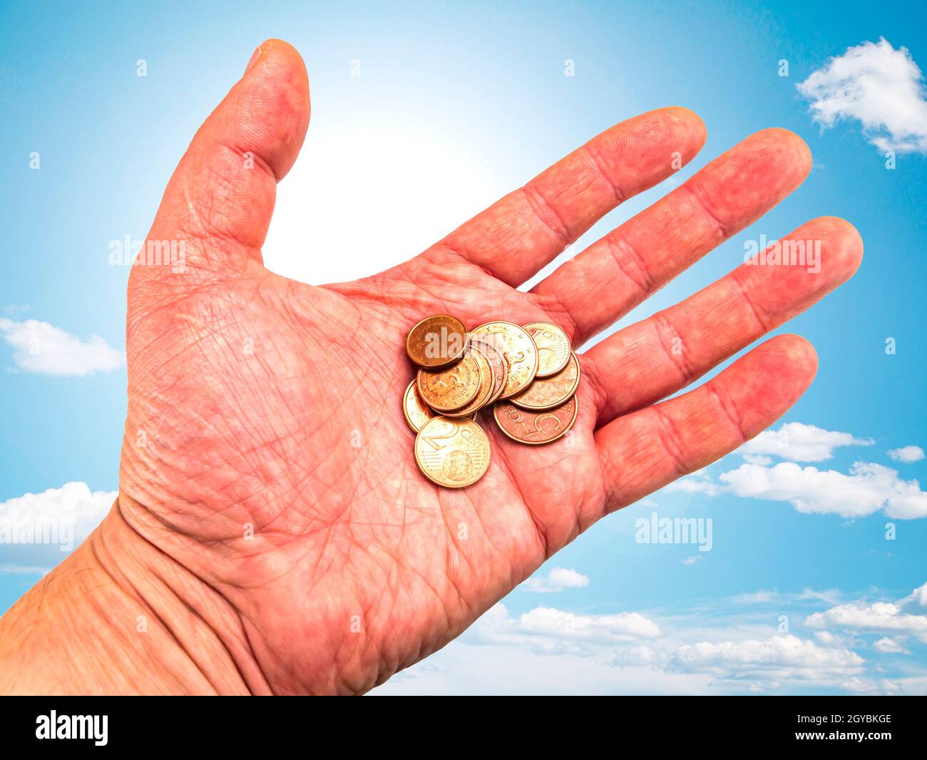 Hand mit Geldmünzen auf einem Hintergrund des blauen Himmels. Gottes Geschenk. Gebet. Bitte um Hilfe. Um Geld bitten. Hand des Gebers. Sonnenstrahlen. Euro-Geld. Backgro Stockfoto