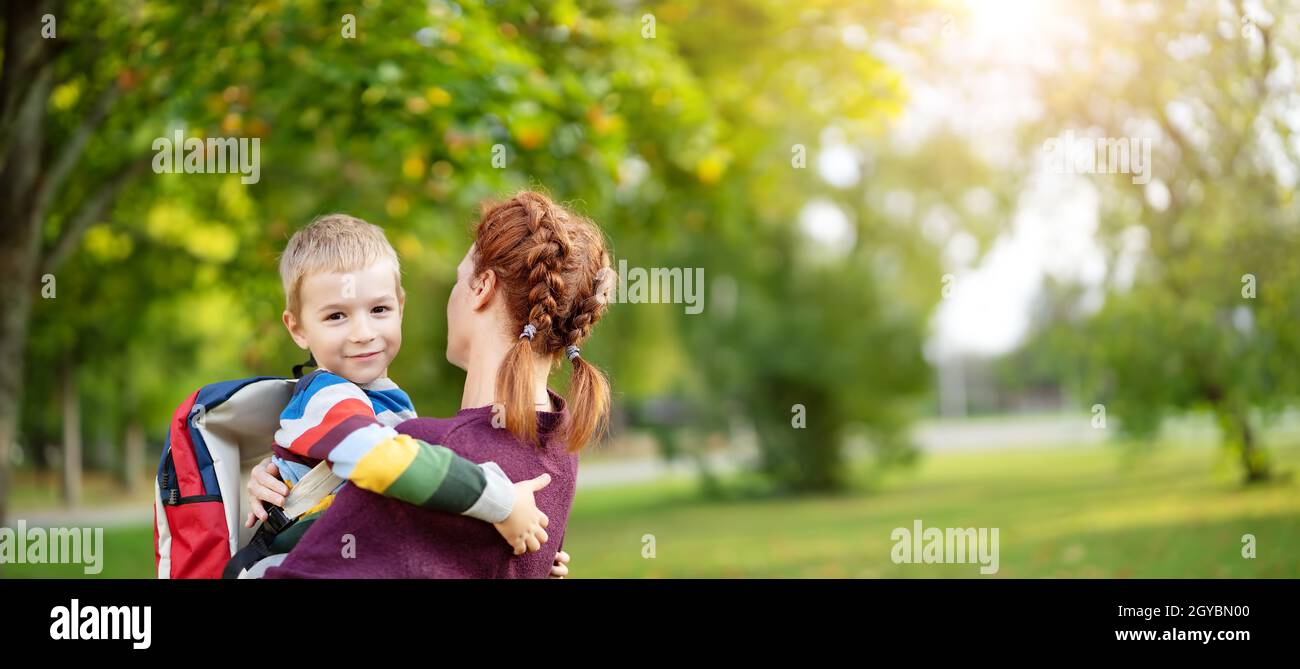 Mutter trifft ihren Sohn von der Grundschule. Umarmen Sie ihr Kind. Das Konzept von Selbstabhängigkeit, Studium und Familienbeziehungen. Stockfoto