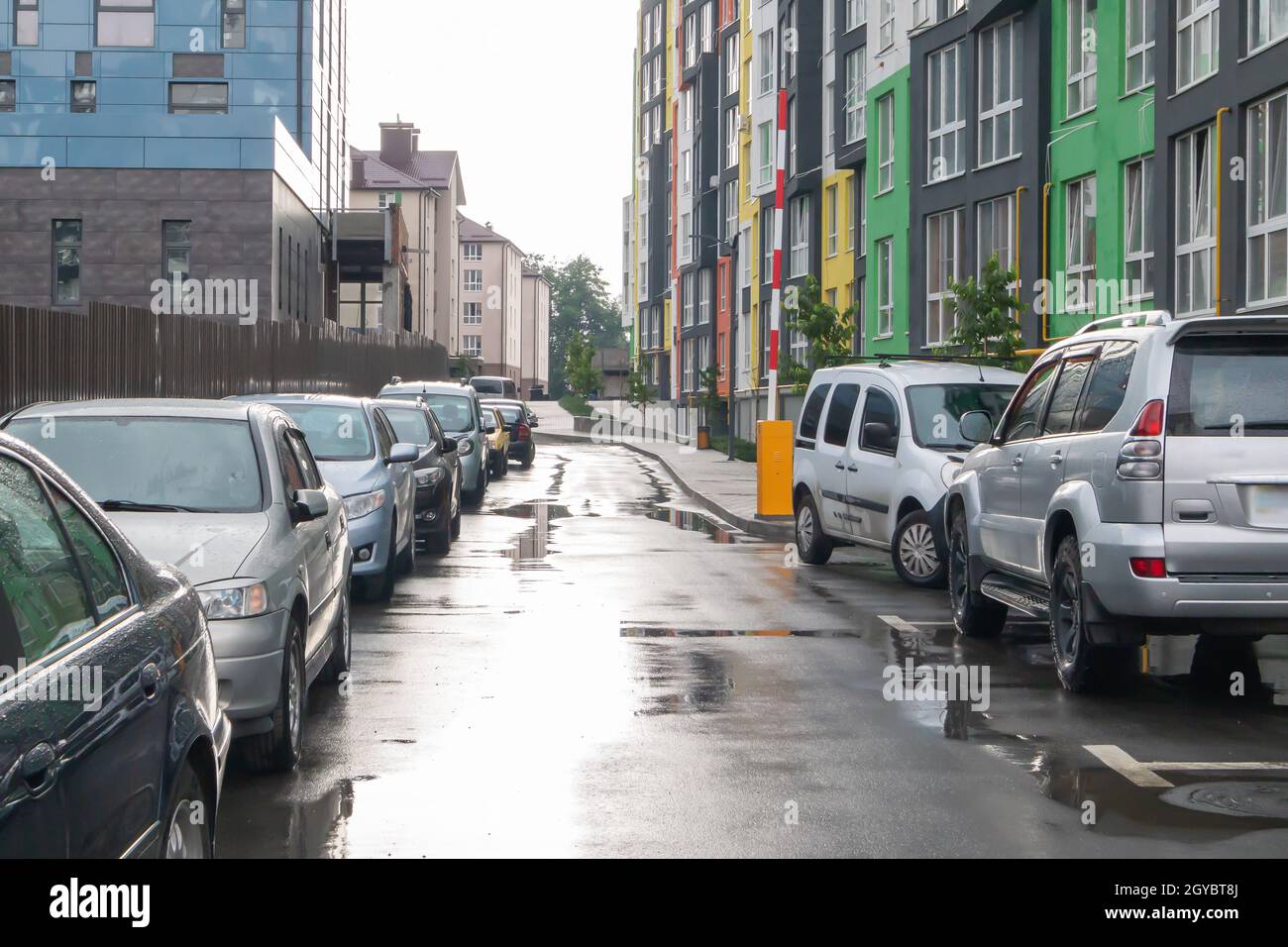 Straße in einer Stadt ohne Menschen mit geparkten Autos bei regnerischem Wetter. Regen auf der Straße. Regen und Autos. Hintergrund von geparkten Autos auf einer regnerischen Stadtstraße. Stockfoto