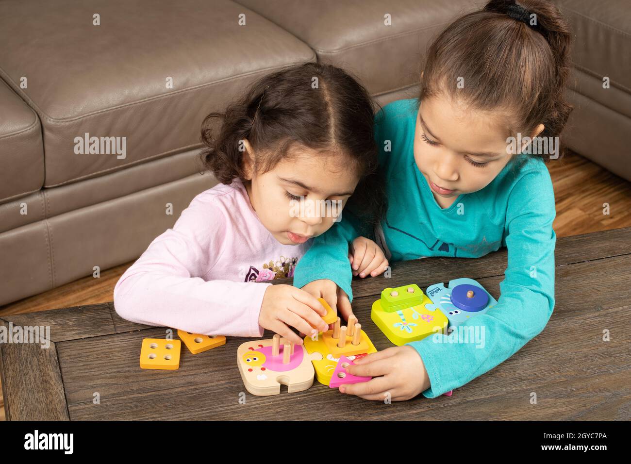 Fünf Jahre altes Mädchen hilft drei Jahre alte Schwester lernen, wie man geometrische Formen Puzzle zu tun Stockfoto