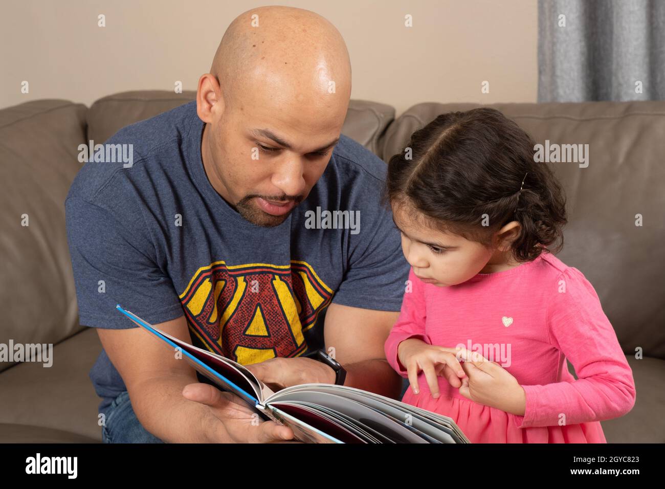 Vater liest zu Hause vor 3-jähriger Tochter Stockfoto