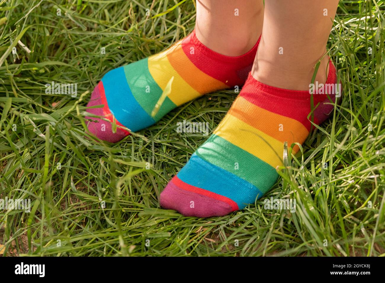 Regenbogensocken auf den Füßen des Mädchens. Kinderfüße in bunten Socken auf dem grünen Gras. Stockfoto