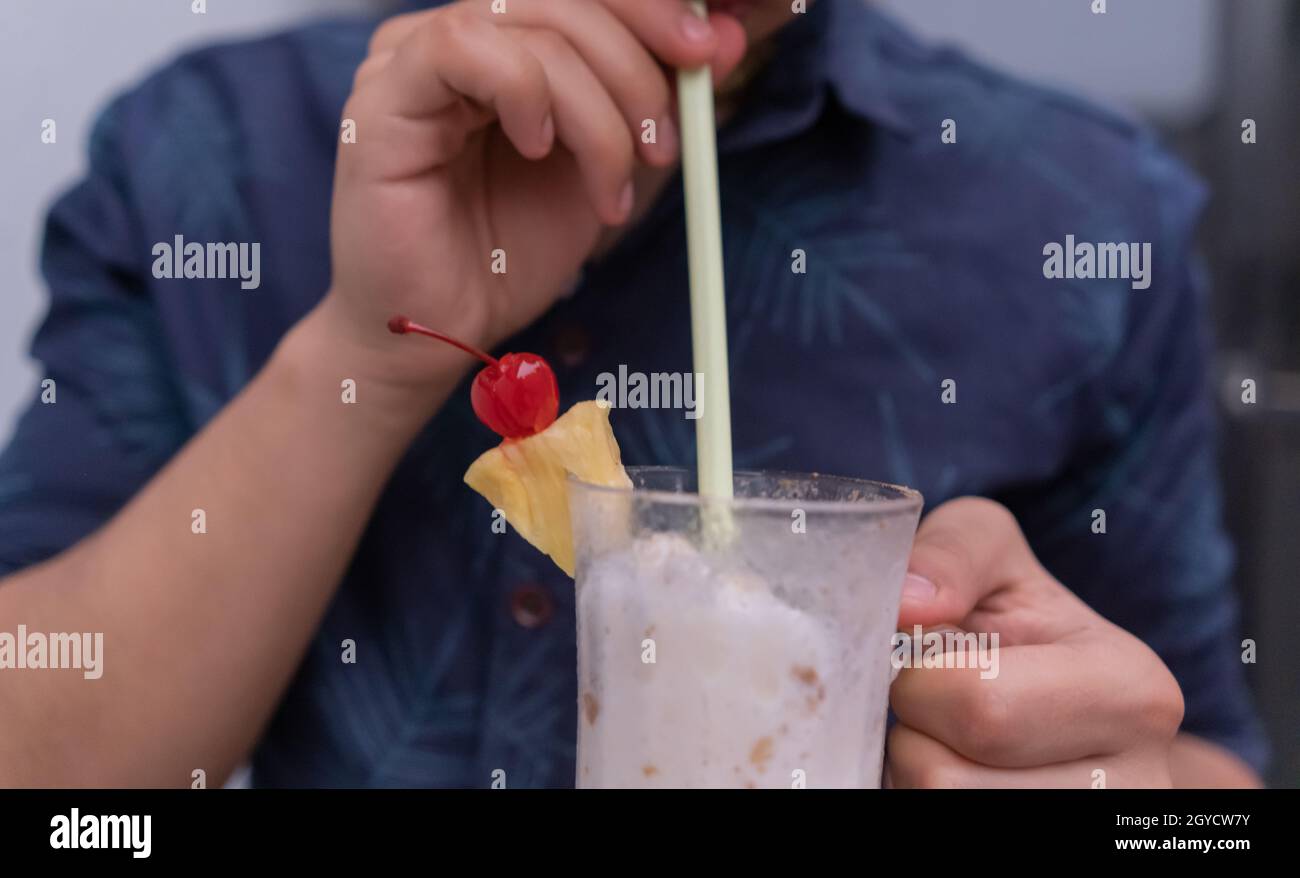 Mann hält und trinkt leckeren Vanillemilchshake mit Stroh Stockfoto