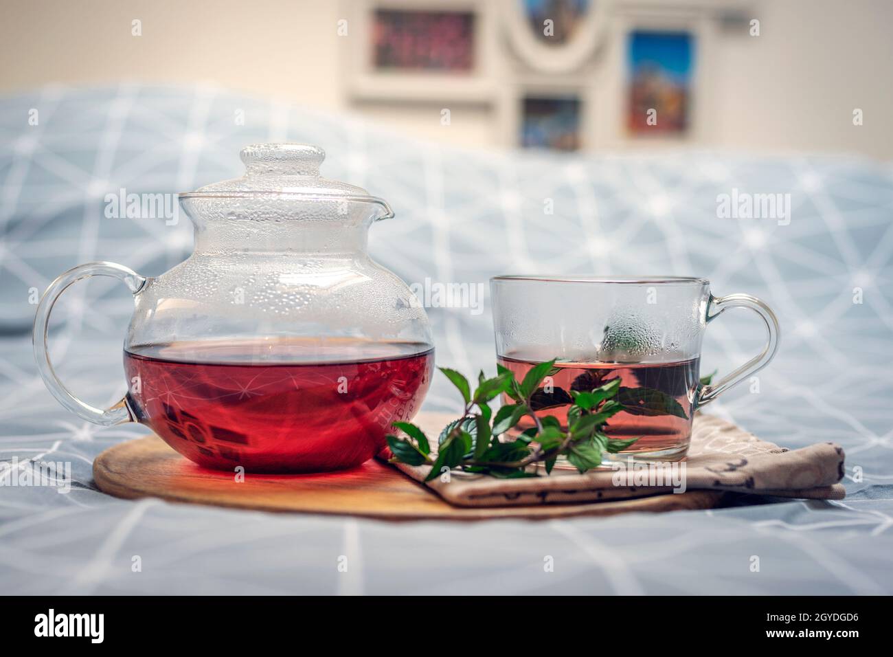 Eine Tasse Kräutertee und Glas Teekannen auf einem Holztablett auf dem Bett. Frühstückskonzept. Nahaufnahme. Stockfoto