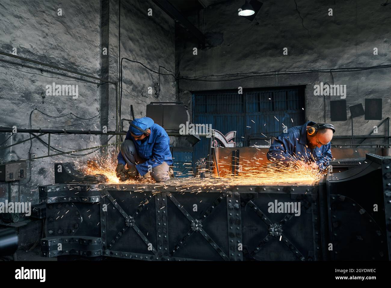 Zwei Industriearbeiter auf einer speziellen Schutzuniform, die beim Zusammenschweißen von Metallrahmen viele Funken erzeugen. Arbeitsprozess bei FORGE. Stockfoto