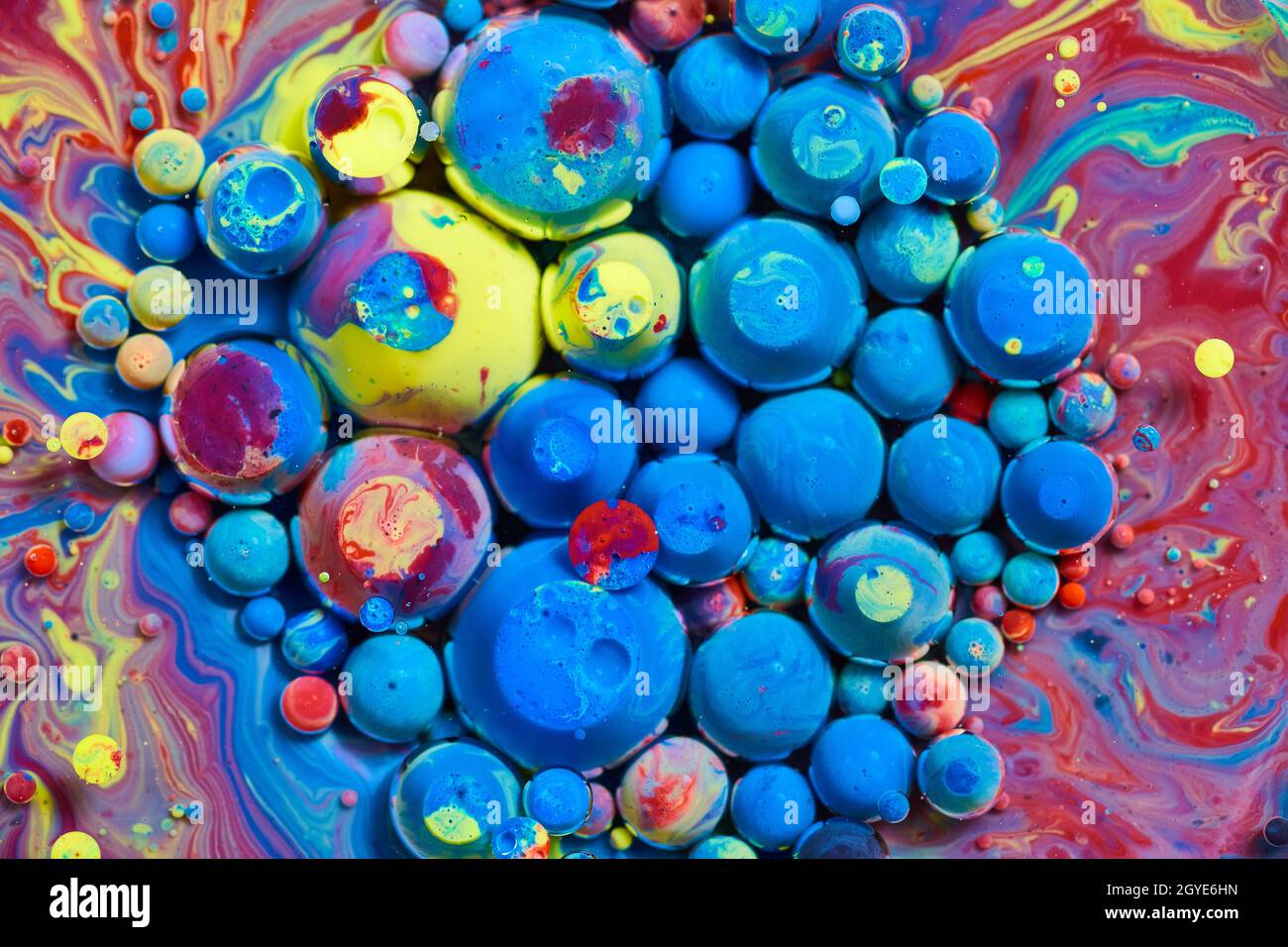 Cluster von blauen und Regenbogenkugeln auf der Oberfläche von farbenfroher Flüssigkeit Stockfoto