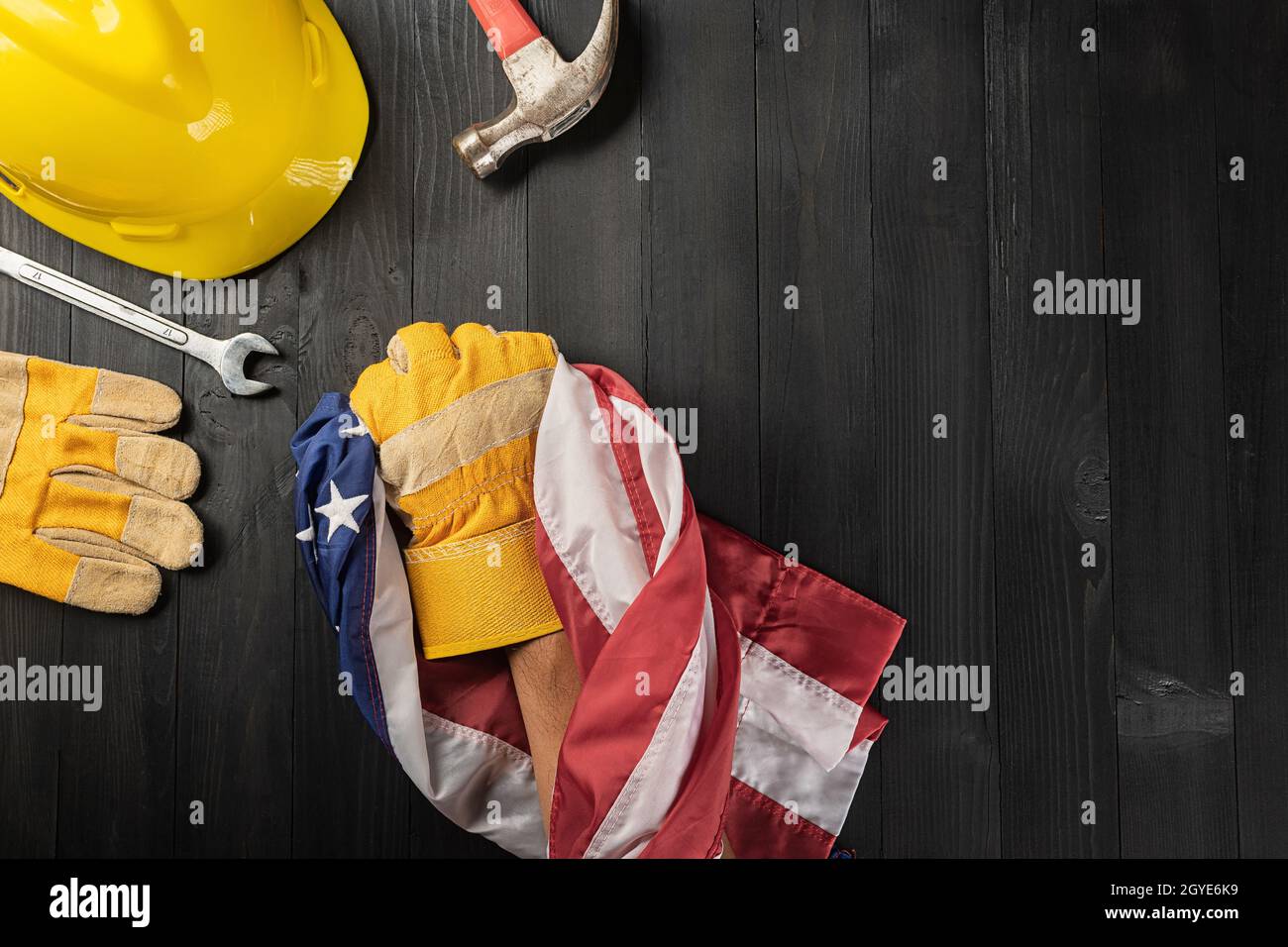 Alles gute zum Labour Day. Mehrere Ingenieur Konstrukteur arbeiten Werkzeuge und , Handschuh hält ergreifende US-amerikanische Flagge mit Kopieplatz auf schwarzem dunklen Hintergrund, gemacht Stockfoto