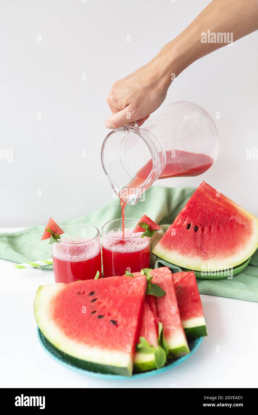 Das Mädchen gießt aus einem Krug frisch gepressten Saft aus frischer Wassermelone, einen gesunden Smoothie aus Wassermelone und Minzblättern Stockfoto