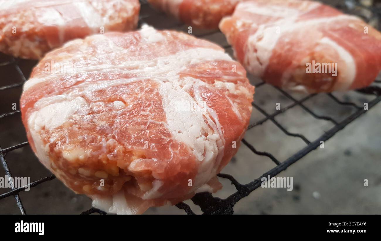 Rohe Fleischschnitzel, die in Speck eingewickelt sind, werden auf dem Grillrost gegarten. Der Küchenchef bereitet die gegrillten Burger-Patties zu. Zutaten für die Herstellung eines Hamburgers. Fleisch Stockfoto