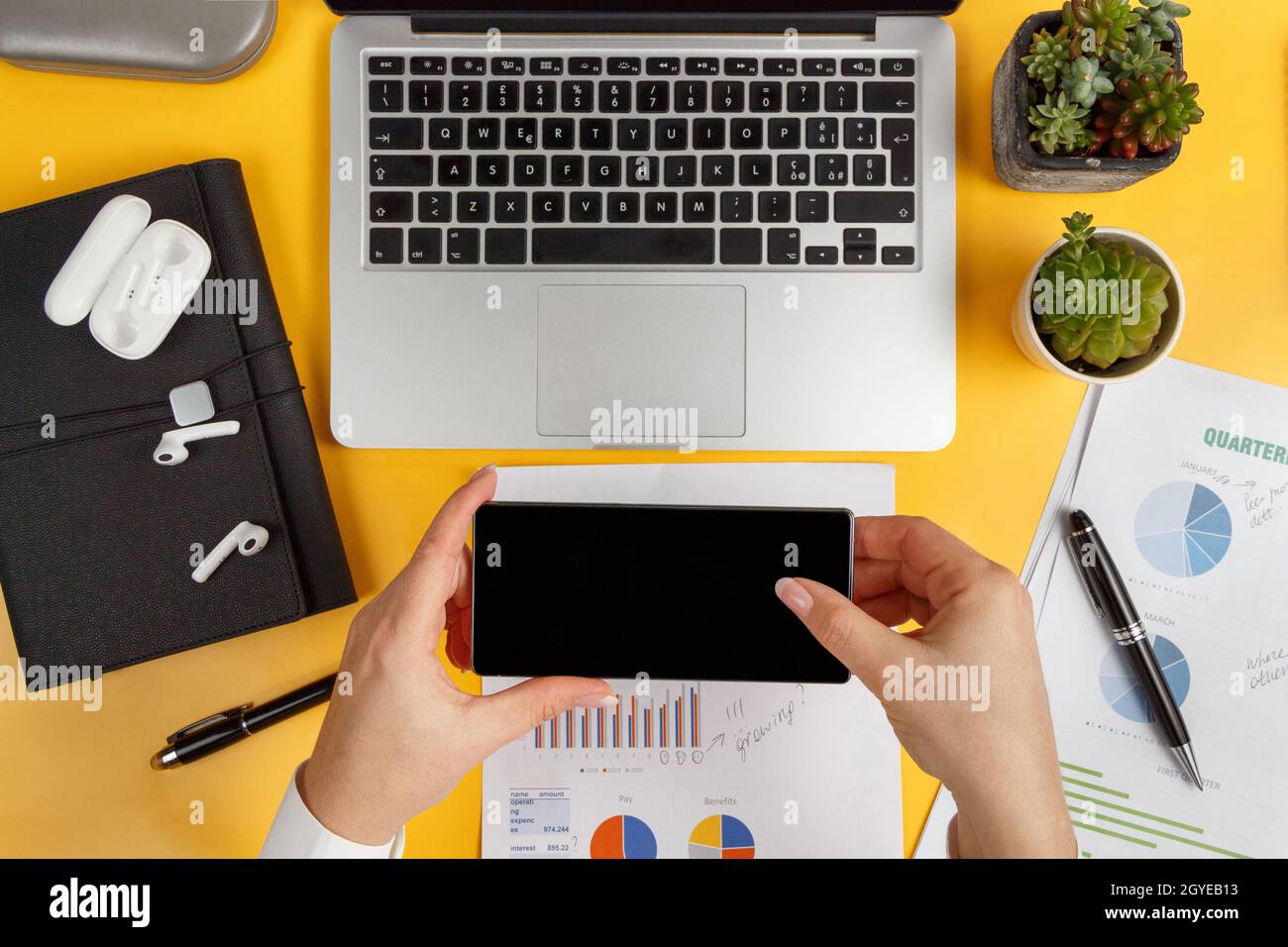 Geschäftsfrau hält Handy in der Nähe von Laptop und berichtet. Blick von oben auf das moderne Büro, gelber Schreibtisch Stockfoto