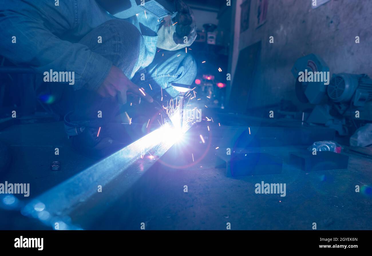 Schweißer schweißen Metall mit Argon-Lichtbogen-Schweißmaschine und hat Schweißfunken. Ein Mann trägt Schweißmaske und Schutzhandschuhe. Sicherheit in der Industrie Stockfoto