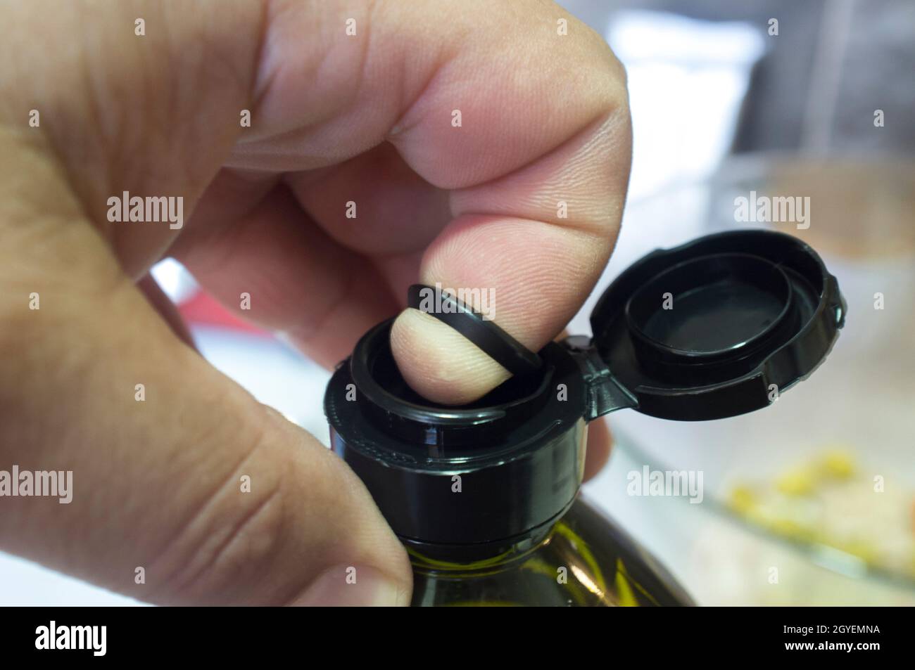 Öffnen einer versiegelten Olivenölflasche mit Finger und einer inneren herausziehbaren Kunststofflasche unter der Kappe. Nahaufnahme Stockfoto