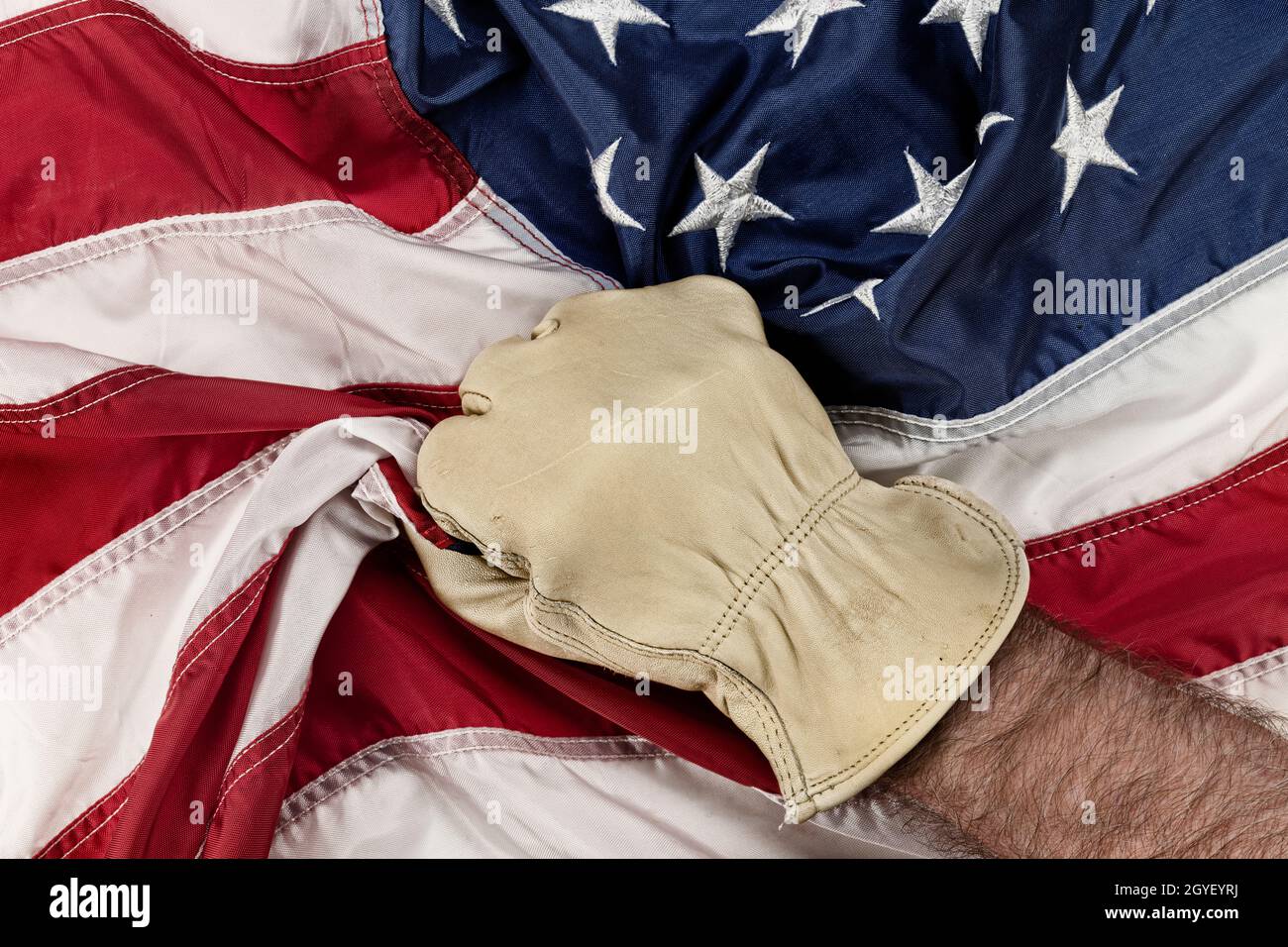 Ein Mann mit Lederhandschuhen greift frustriert und wütend die amerikanische Flagge, während die Regierungspolitik Jobs mit blauem Kragen ins Ausland verlegt. Stockfoto