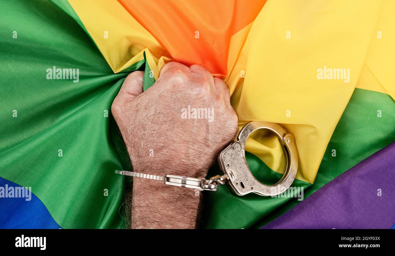 Ein Mann in Handschellen ergreift die LGBTQ-Regenbogenfahne in Frustration und Wut, während Unterdrückung und Bürokratie die Akzeptanz behindern Stockfoto