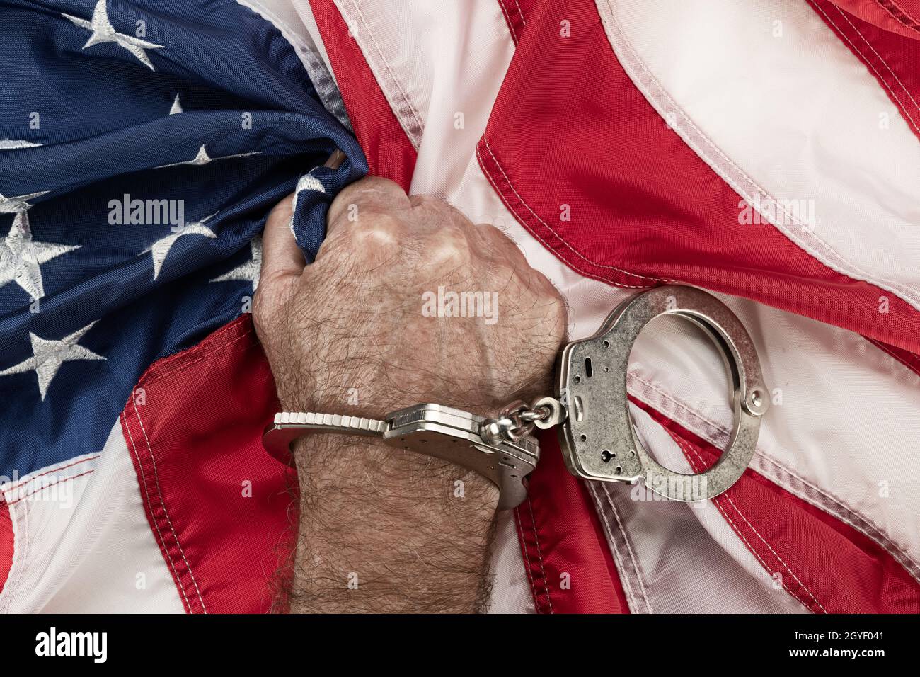 Ein Mann in Handschellen greift frustriert und wütend die amerikanische Flagge, während Unterdrückung und Bürokratie seine Freiheit verhindern. Stockfoto