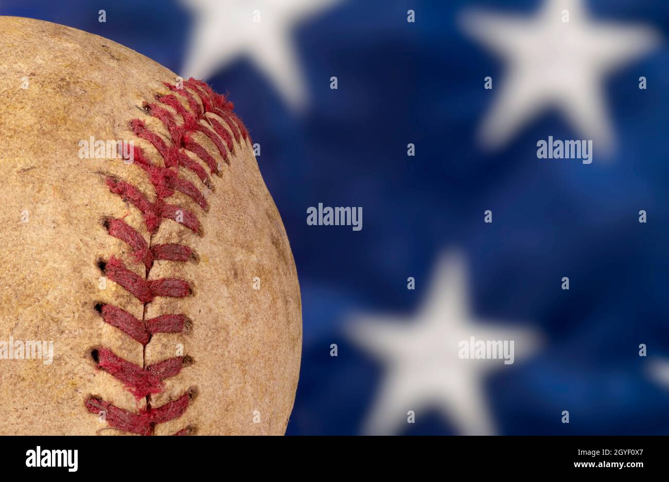 Nahaufnahme eines alten, gebrauchten Baseballs gegen eine amerikanische Flagge, die den nationalen Zeitvertreib der Vereinigten Staaten hervorhebt. Stockfoto