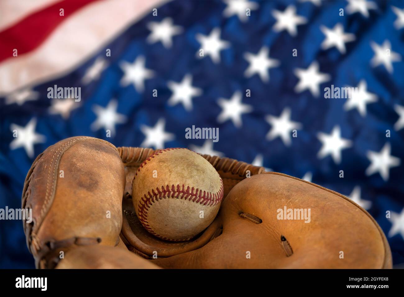 Die Nahaufnahme eines alten Baseballs und der Handschuh gegen die amerikanische Flagge zeigen eine der beliebtesten Sportarten des Landes. Stockfoto