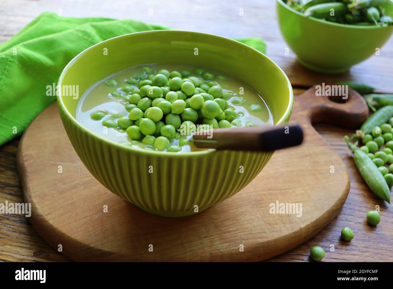 Frische grüne Erbsensuppe mit Erbsensamen und Erbsenschoten herum. Selektiver Fokus, Fokus auf die Erbse in der Mitte der Suppe. Stockfoto