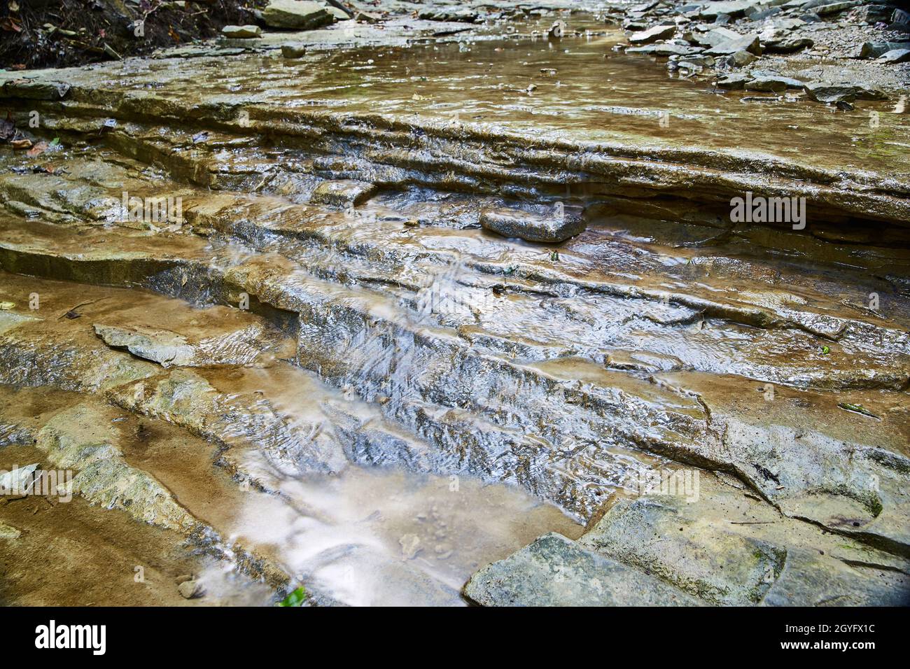 Das Wasser fließt sanft über einen steinigen Grund eines flachen Wasserbeckens, der kleine Wasserfälle bildet Stockfoto