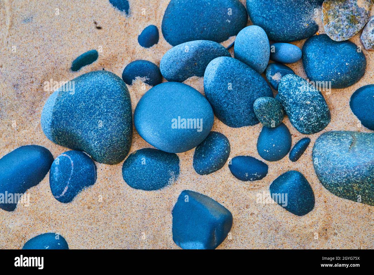 Blaue und schwarze Steine an einem Sandstrand Stockfoto