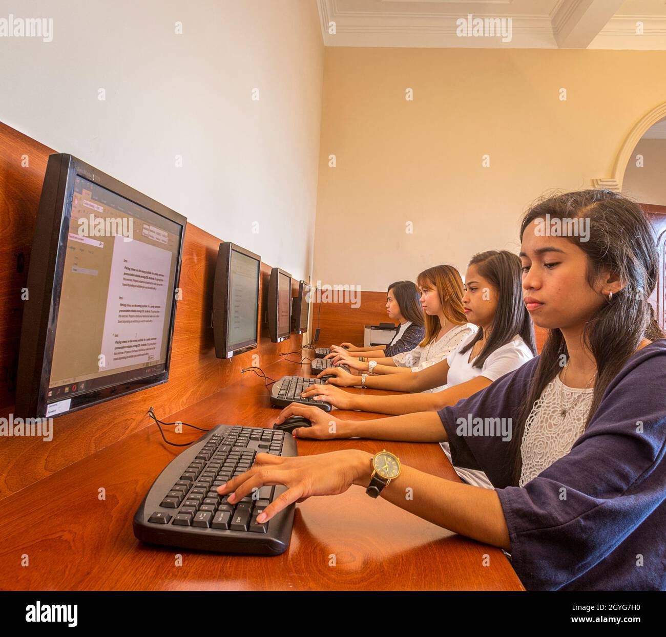 Langer Schreibtisch mit Computermonitoren und Studenten, die den Bildschirm mit Tastaturen lesen. Stockfoto