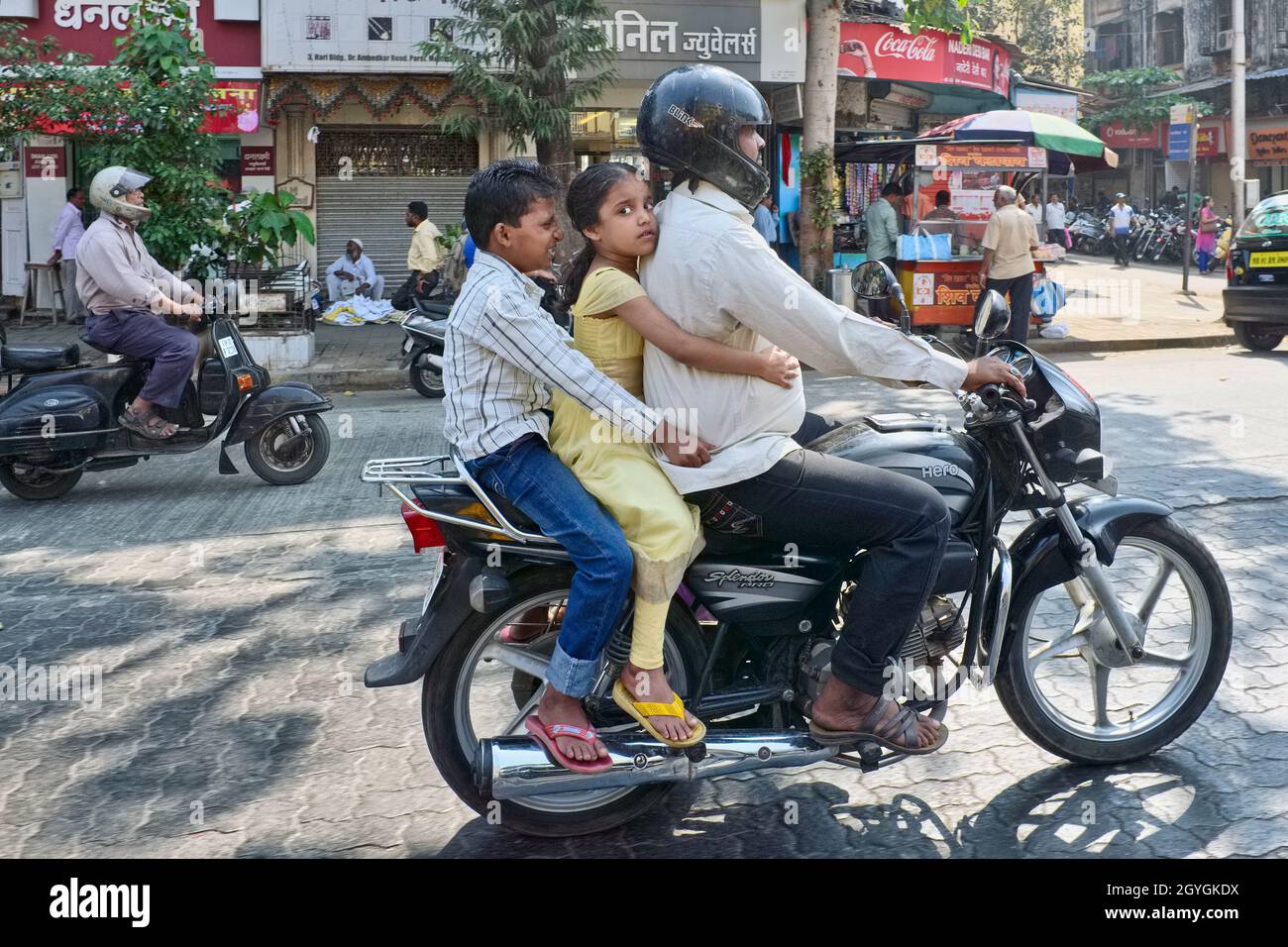 Ein Vater, der mit seiner jungen Tochter und seinem Sohn auf dem Motorrad unterwegs ist und sich an ihm festhält, fährt auf einem Sozius, Mumbai (Bombay), Indien Stockfoto