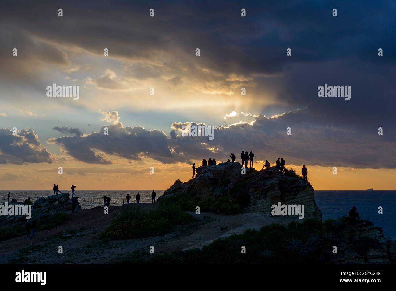 LIBANON, BEIRUT, RAS BEYROUTH, TOURISTEN UND LIBANESEN AUF EINEM FELSEN AM MEER BEI SONNENUNTERGANG IN DER NÄHE VON TAUBENFELSEN (RAOUCHE) Stockfoto