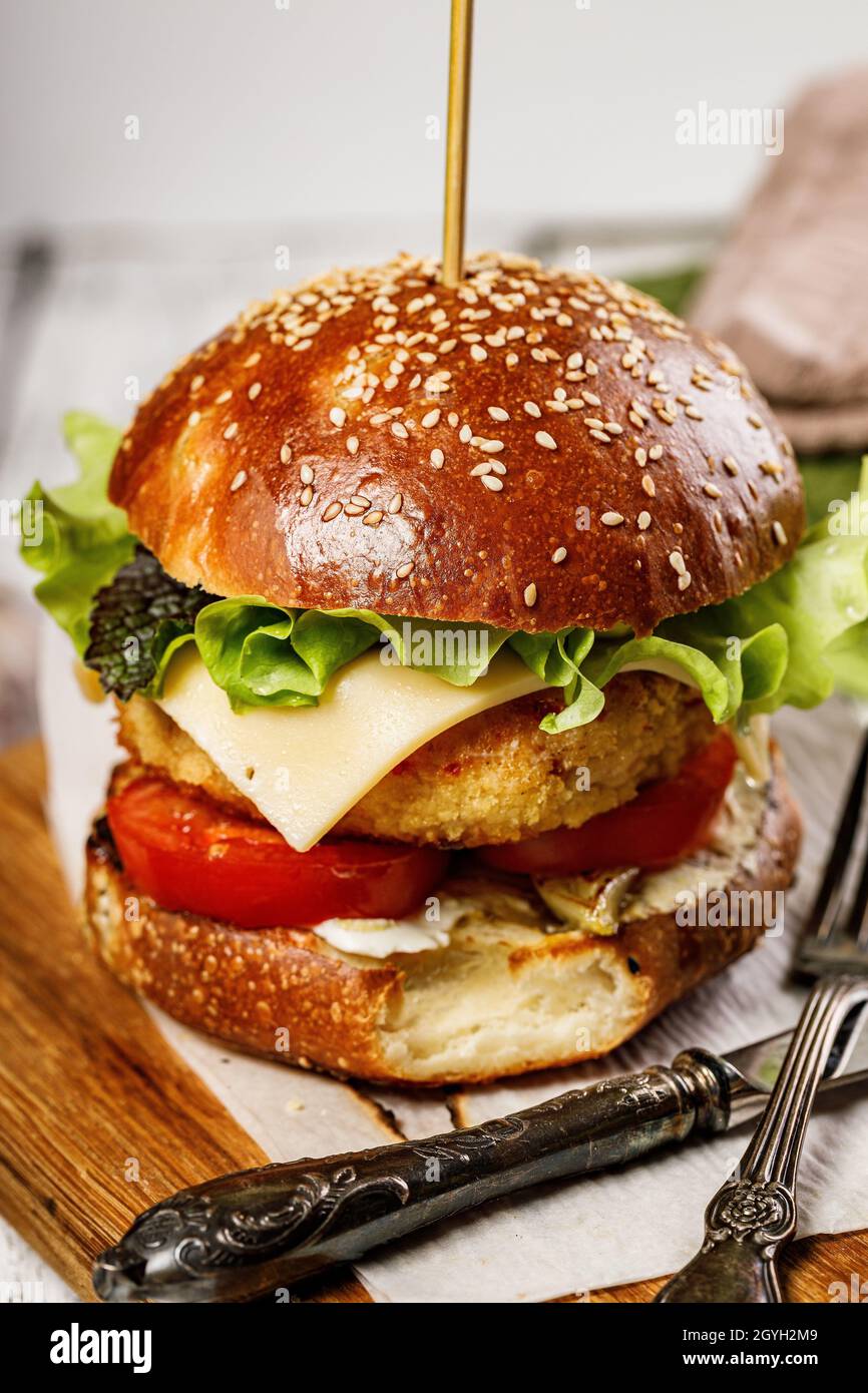 Appetitliche Hähnchenburger mit Käse, frischem Salat und Gemüse. Frische Salatblätter, Tomaten und Zwiebeln. Köstliche traditionelle amerikanische Küche. Whi Stockfoto
