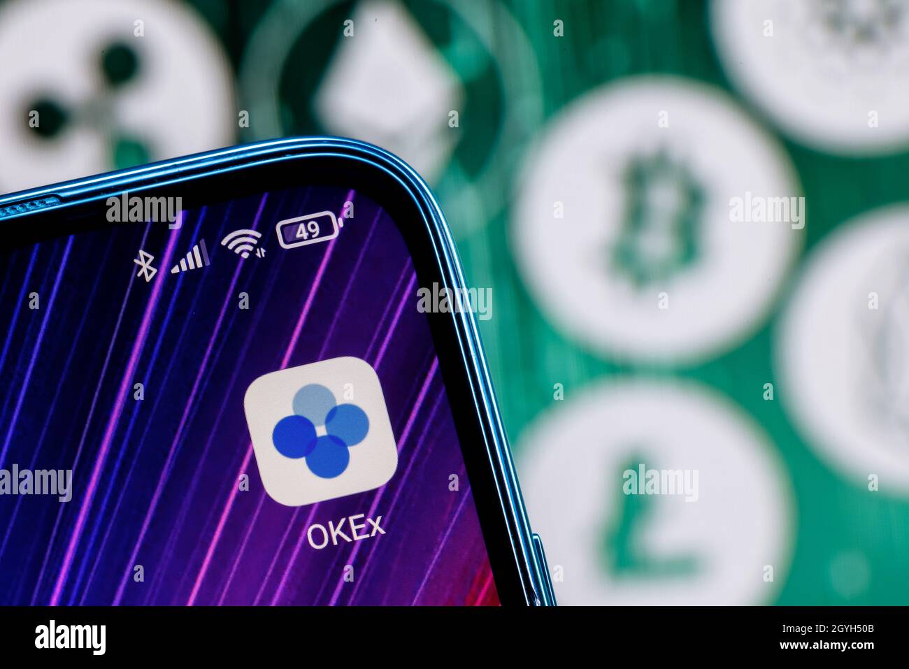 OKEx ist eine Kryptowährungsbörse. OKEx App auf dem Smartphone-Bildschirm vor dem Hintergrund der wichtigsten Kryptowährungen. Stockfoto