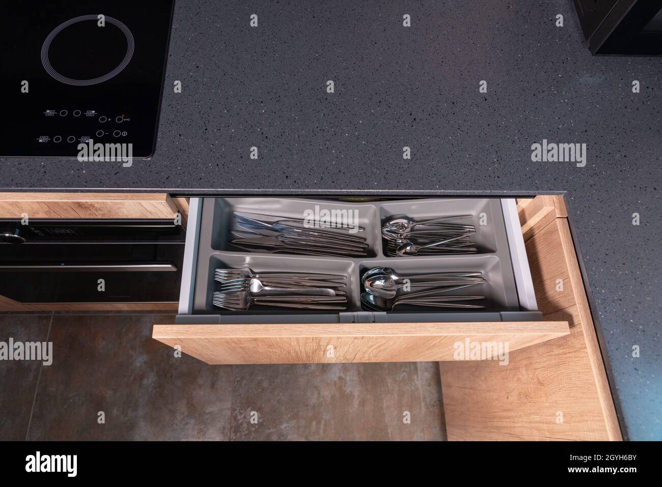 Draufsicht auf eine Küchentheke aus grauem Stein mit offener Besteckschublade, in der die Essgeschirr übersichtlich in Fächern mit Stauraum angeordnet sind Stockfoto