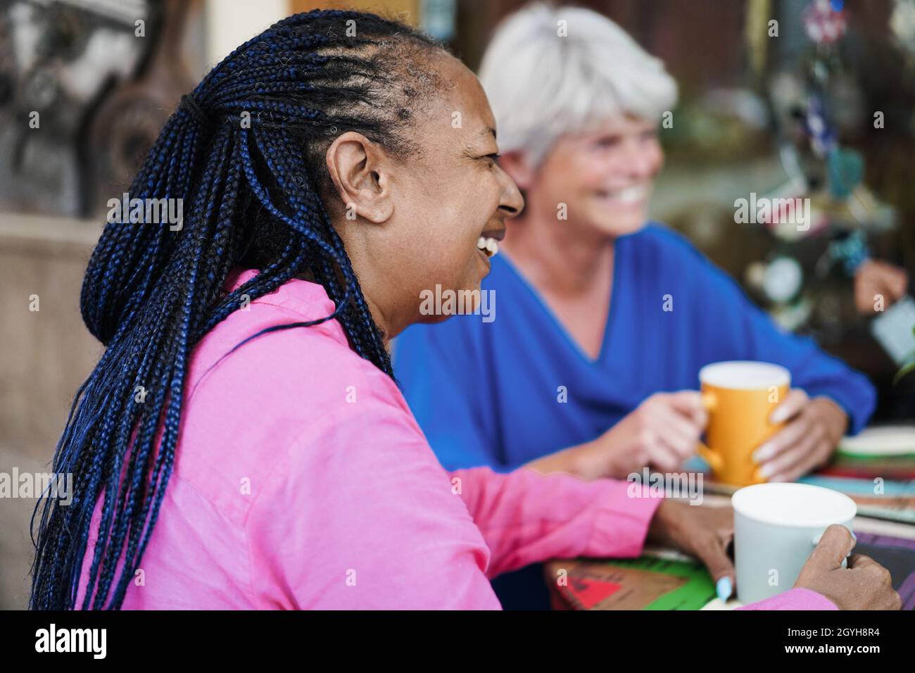 Ältere Freunde aus verschiedenen Rassen treffen sich und unterhalten sich an der Bar im Freien, während sie gemeinsam Kaffee trinken Stockfoto